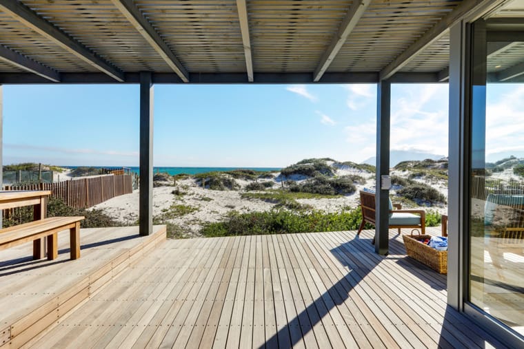 The covered deck with a timber bench and table, facing the dune and sea